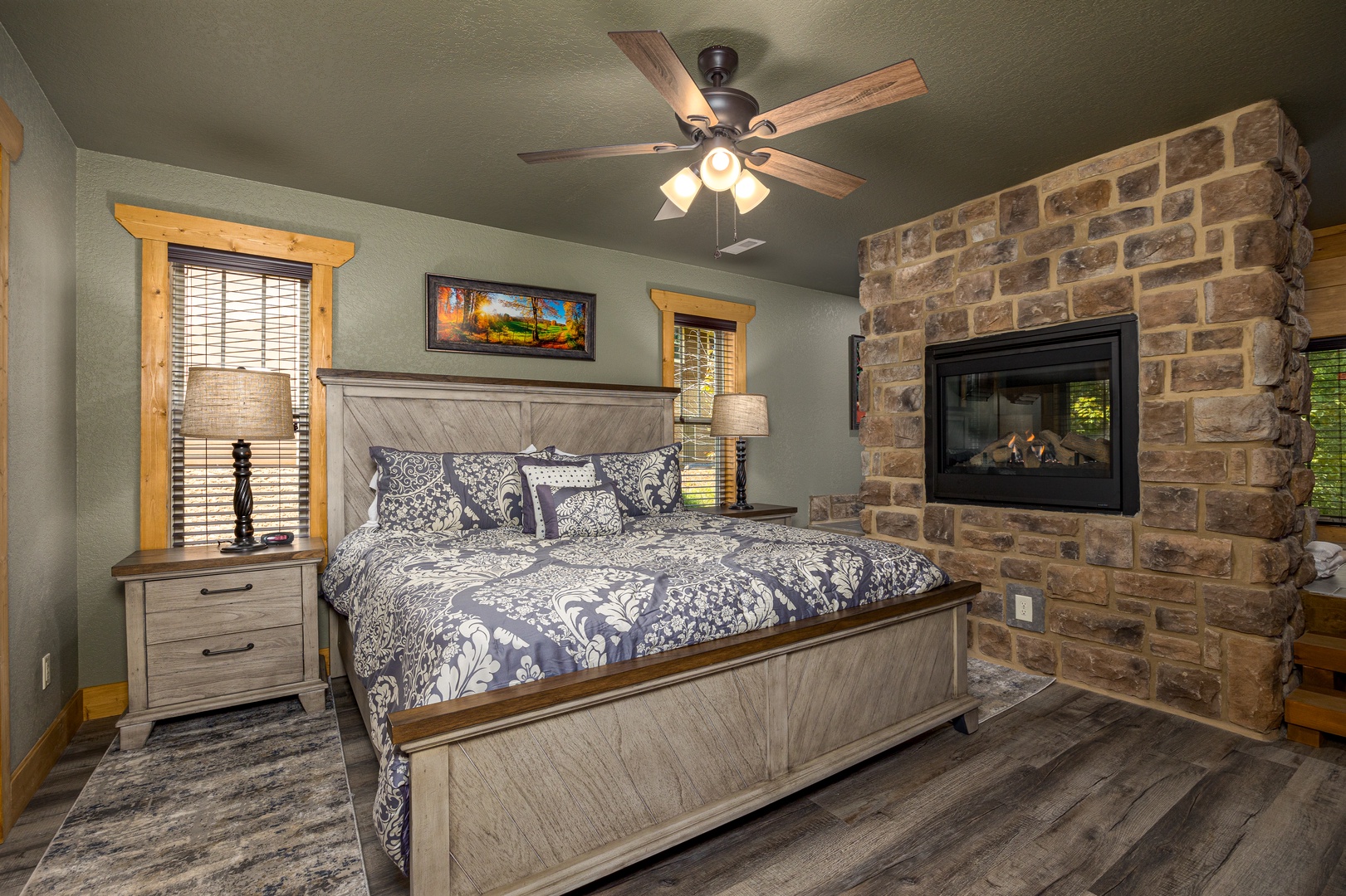 Southern Comfort master bedroom — king bed, stone gas fireplace, hardwood floors, and cedar trim at Laurel Estates at The Glades
