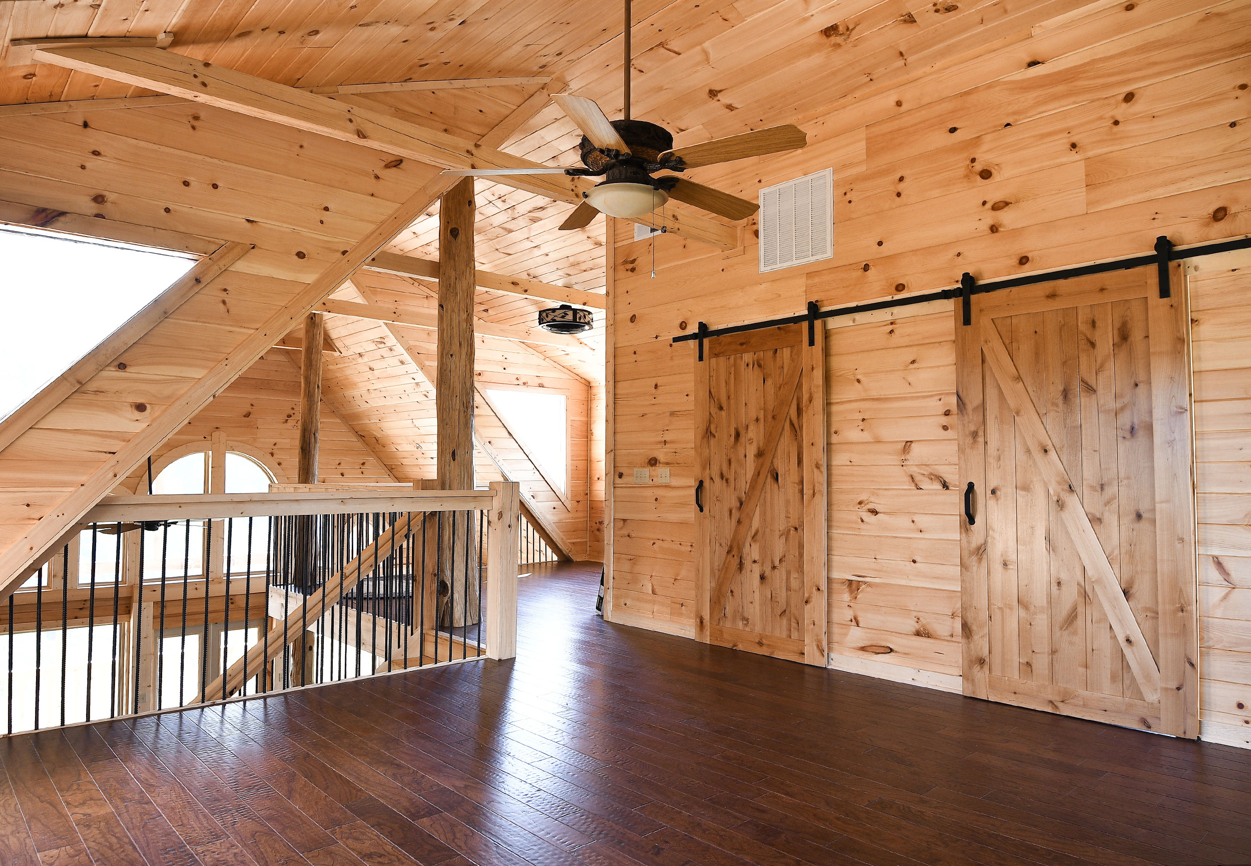 Cabin loft interior — tongue-and-groove pine ceiling, barn sliding doors, dark hardwood floors, and open staircase at Laurel Estates