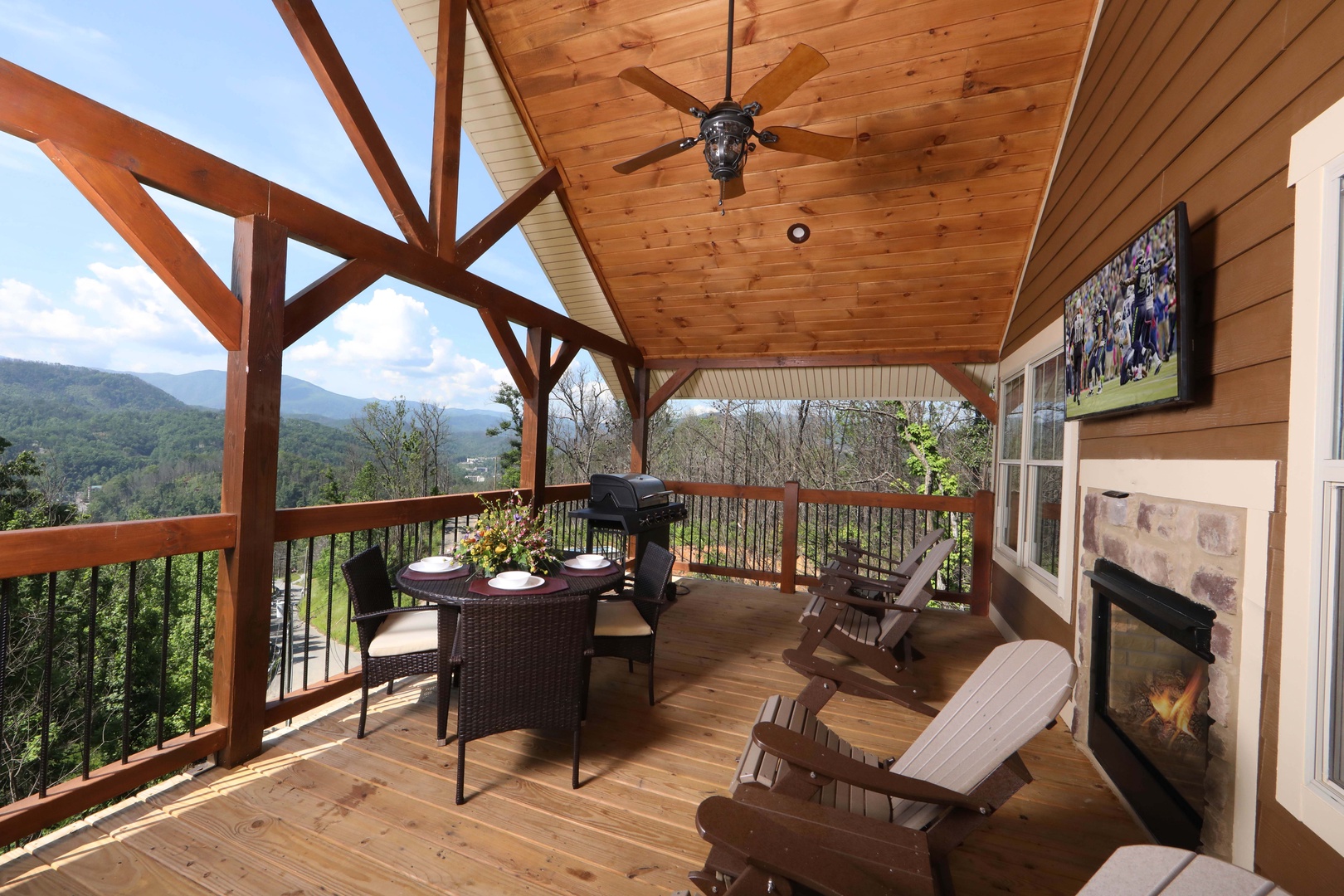 Above It All covered outdoor deck — panoramic Smoky Mountain views, stone outdoor fireplace, dining area, Adirondack chairs, and outdoor TV at Laurel Estates